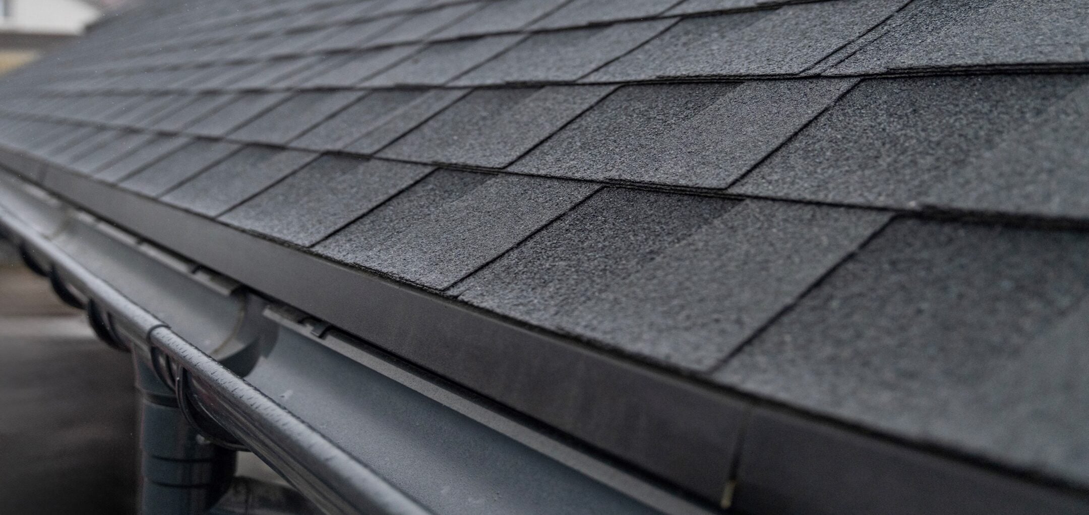 Dark gray asphalt roof shingles with rain gutter system close up