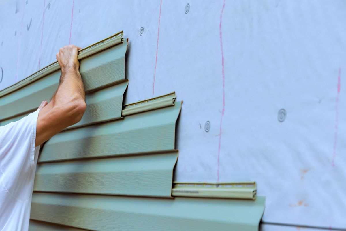 Construction worker carefully places installing new pvc vinyl siding siding panels on building exterior wall