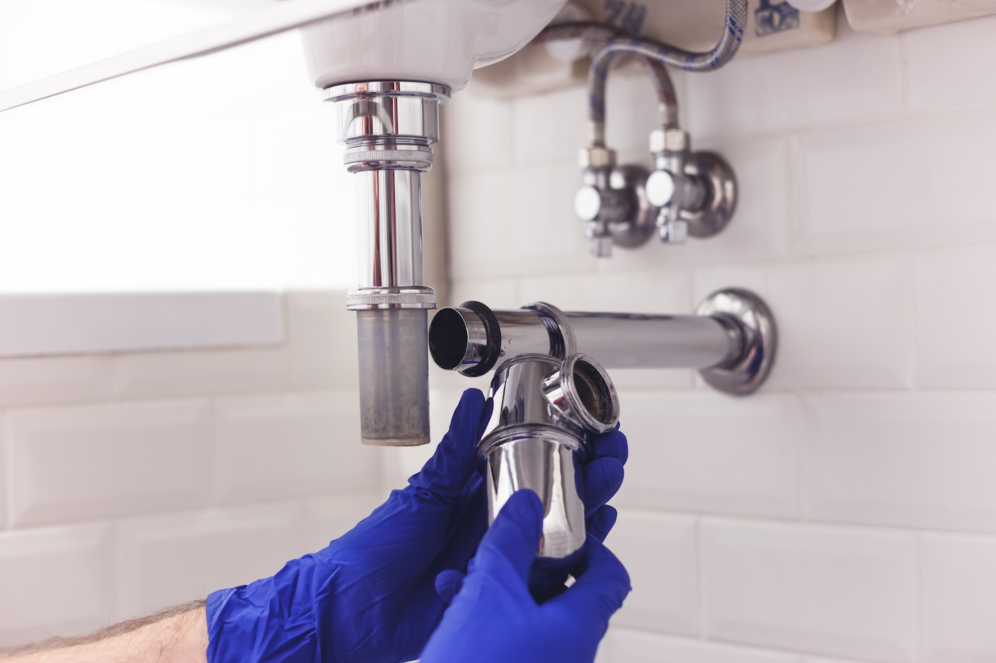 Plumber repairs and maintains chrome siphon under the washbasin. Plumber at work in bathroom, plumbing assemble and install concept.